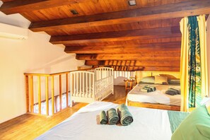 Une pièce avec un plafond en bois, un berceau, un lit avec des serviettes enroulées et un escalier.
