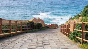 Un sendero pavimentado que lleva al mar, con barandas de madera y vista al océano.