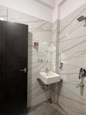A bathroom with a dark wooden door, a white sink, a mirror, and a shower. - Renee Mysaa (Indore)