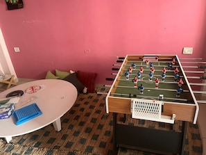 A room with a foosball table, a round table with a blue tray, and a patterned carpet. - Renee Mysaa (Indore)
