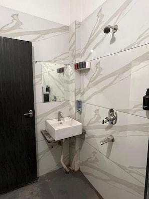 A bathroom with a white sink, a mirror, a shower, and a dark door. - Renee Mysaa (Indore)