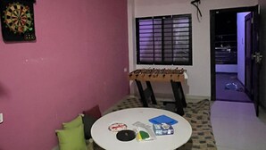 Ein Zimmer mit Deckenventilator, Dartscheibe, Tisch mit diversen Gegenständen und Fenster mit Jalousien.