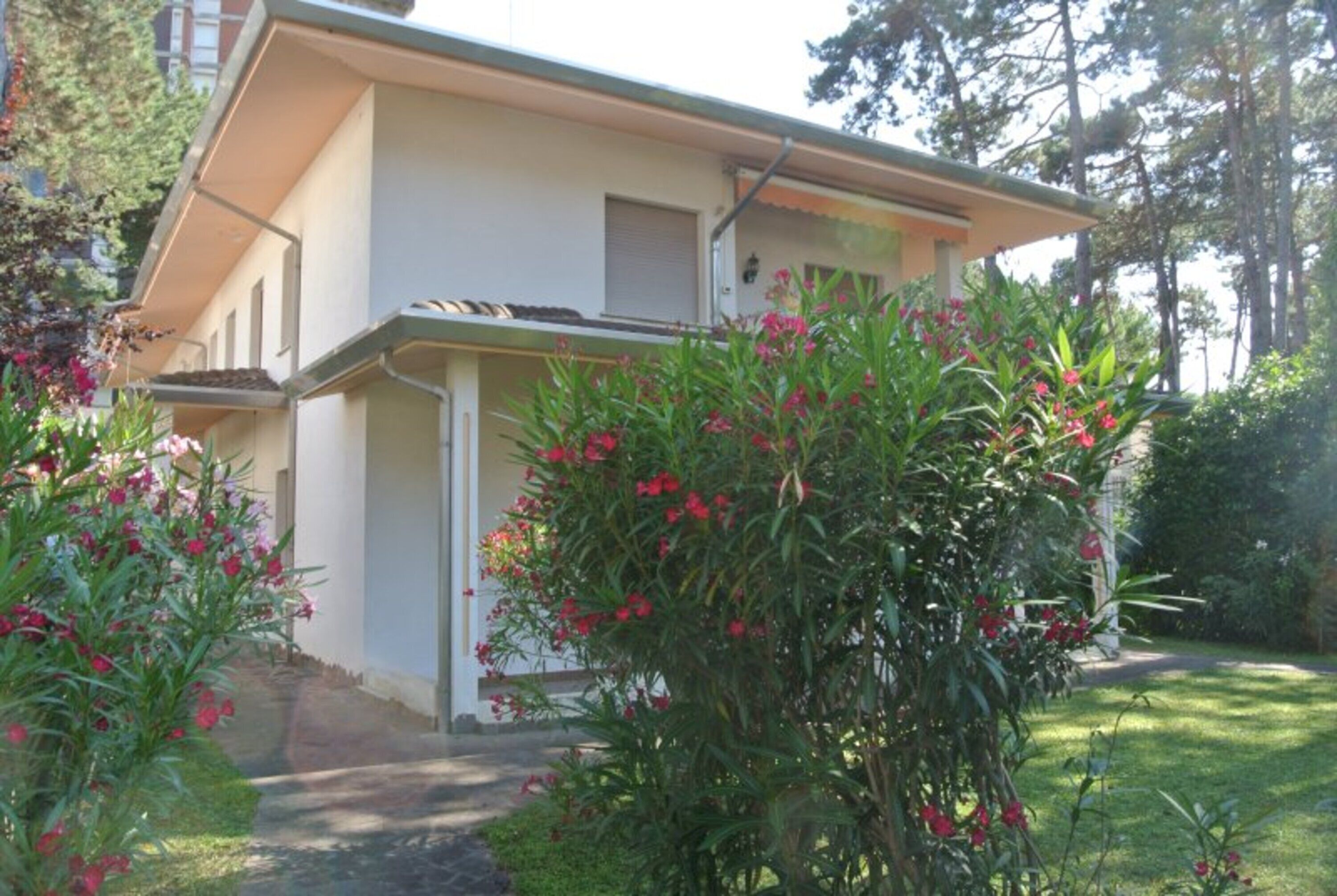 A two-story building with a balcony, surrounded by lush greenery and flowering plants.