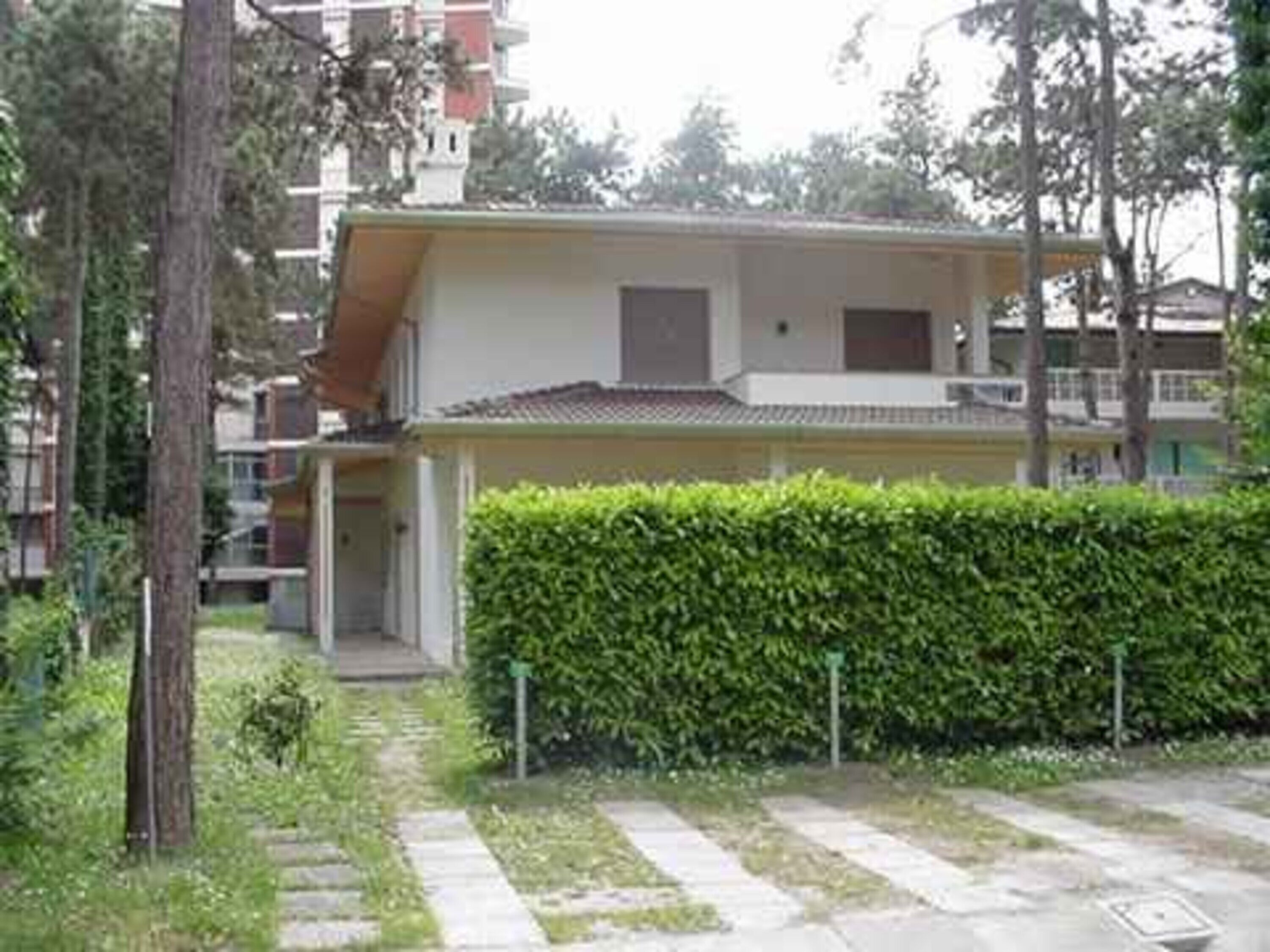 A residential building with a flat roof, a visible entrance, and a well-maintained hedge in front.