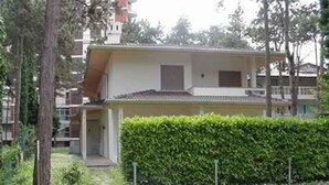 Ein Wohngebäude mit flachem Dach, einer gut sichtbaren Eingangstür und einem gepflegten Heckenstreifen davor.