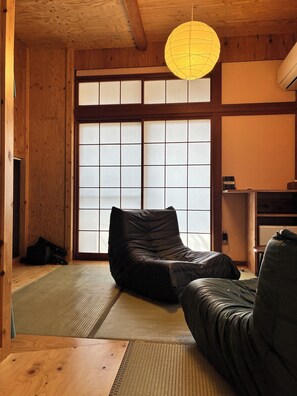 A traditional Japanese room with tatami flooring, a black sofa, a wooden ceiling, and a sliding shoji door. - Guesthouse Mitaki (Hiroshima)