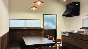 Een moderne eetruimte met een houten tafel en stoelen, hanglampen, een bank en een keuken met een fornuis en afzuigkap.