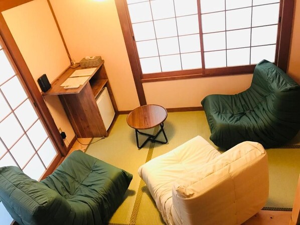Tatami-mattoilla päällystetty huone, jossa on matala pöytä, kaksi vihreää tuolia ja valkoinen sohva.