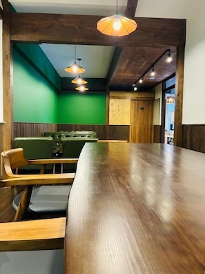 Um restaurante com uma longa mesa de madeira, paredes verdes e luminárias pendentes.