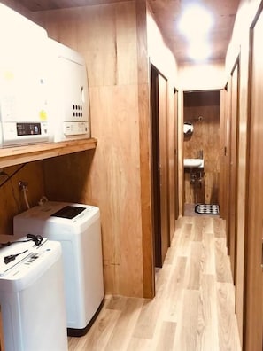 A narrow hallway with wooden walls and a wooden floor. There are two white appliances, possibly washers, on the left. A sink is visible in the distance. - Guesthouse Mitaki (Hiroshima mitaki honmachi)
