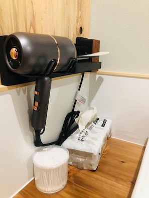 A hair dryer mounted on a wall, a white container, and a package of tissues. - Guesthouse Mitaki (Hiroshima mitaki honmachi)