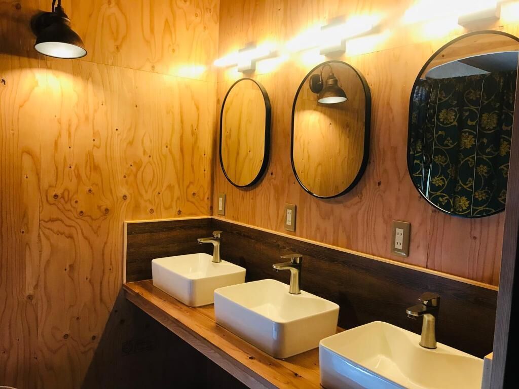A wooden wall with three white sinks and overhead lighting.