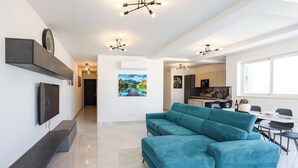 Een moderne woonkamer met een blauwgroene bank, een flatscreen-tv en een eethoek met een tafel en stoelen.