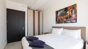 Een hotelkamer met een bed, nachtkastje, deur en een schilderij aan de muur.