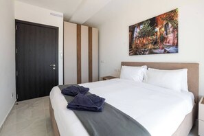 A hotel room with a bed, a nightstand, a door, and a painting on the wall. - Enjoy a bright 3-bedroom, 2-bathroom apartment on the 4th floor with lift access in St Paul’s Bay. Featuring a spacious living area, modern kitchen, balcony/terrace, sea views, and air conditioning, it is ideal for families and groups. (St. Paul's Bay)