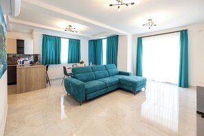 Una sala de estar moderna con un sofá seccional color turquesa, una cocina con encimera de mármol y ventanas amplias con cortinas color turquesa.