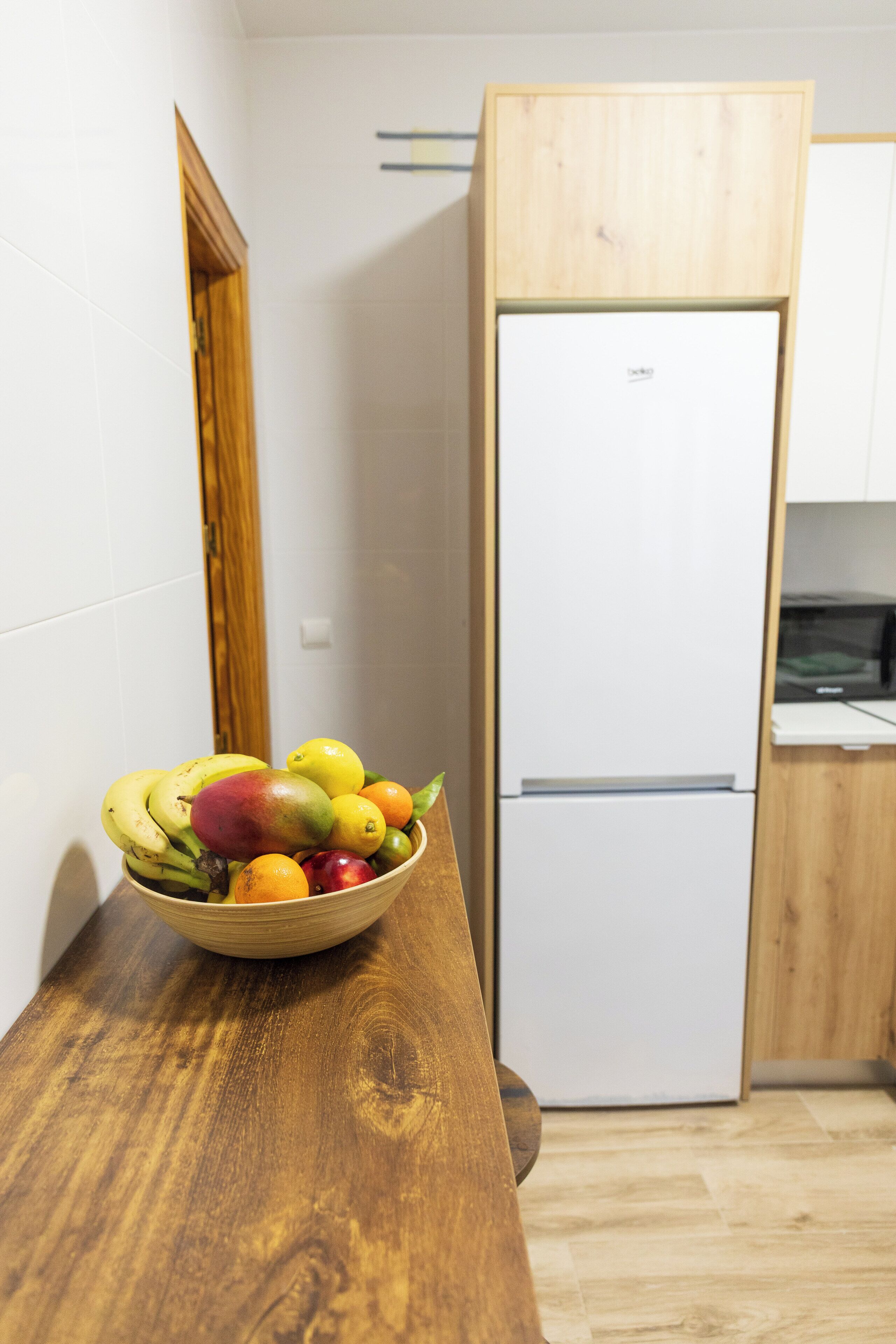 Una cocina con un refrigerador blanco, una encimera de madera y un cuenco de fruta.