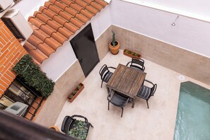 An outdoor patio with a wooden table and chairs, a potted plant, a small pool, and a tiled roof. - Vrbo Property (Torrijos)