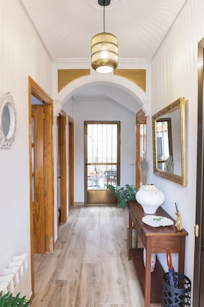 A hallway with wooden doors, a white vase, a mirror, and a ceiling light fixture.