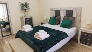 A neatly made bed with a green blanket and pillows, a bedside table with a lamp, a mirror, and a decorative plant. - LODGING IN TORRIJOS TOLEDO ALOJAMIENTO TURISTICO DON PEDRO TOLEDO (Torrijos)