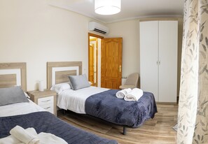 A bedroom with two beds, a wardrobe, a chair, and an air conditioning unit. - Vrbo Property (Torrijos)