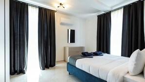 Een moderne hotelkamer met een groot bed, donkere gordijnen, een witte airconditioning en een schone betegelde vloer.