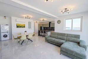 Ein modernes Wohnzimmer mit einer Couch, einem Esstisch, Stühlen, einer Waschmaschine und einer Küche im Hintergrund.