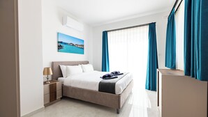 Une chambre d’hôtel moderne, équipée d’un lit, d’une table de chevet, d’un bureau et offrant une vue sur la mer à travers les rideaux.