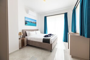 Ein modernes Hotelzimmer mit Bett, Nachttisch, Schreibtisch und Meerblick durch Vorhänge.