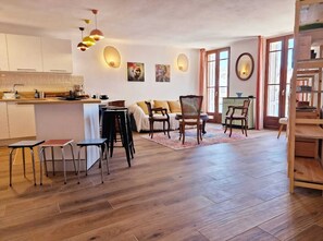 A spacious living area with a kitchen, wooden flooring, and a dining set. - Vrbo Property (La Ciotat)