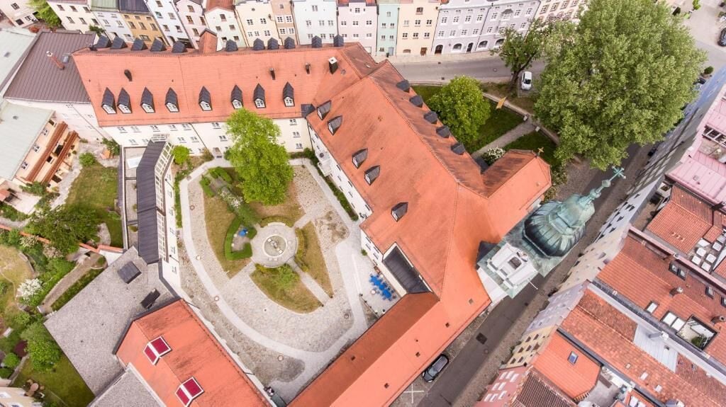 Vista aérea de um edifício com um pátio central, uma estátua e uma estrutura com telhado vermelho.
