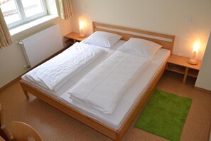 Una cama doble con ropa blanca, dos mesitas de noche con lámparas, un radiador y una alfombra verde.