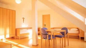 A room with a bed, a desk, and a chair, a cross on the wall, and a staircase.