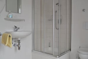 A bathroom with a glass-enclosed shower, a sink with a yellow towel, and a toilet.