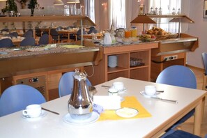 Un bufé de desayuno con una cafetera, tazas y un mantel individual amarillo sobre una mesa.