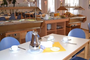 A breakfast buffet with a coffee pot, cups, and a yellow placemat on a table.