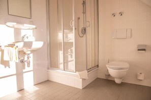 Baño con cabina de ducha de vidrio, inodoro y lavamanos.