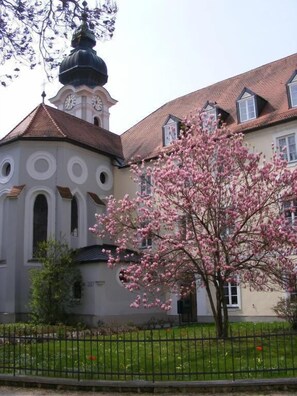 A building with a clock tower, a large tree with pink blossoms, and a well-maintained lawn.
