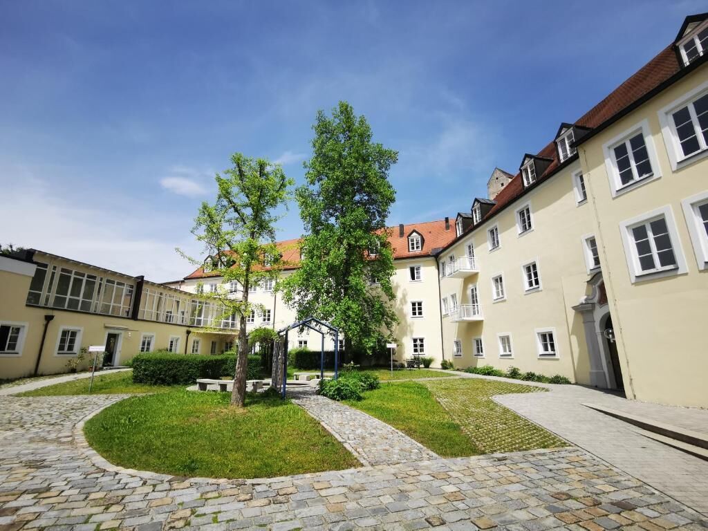 A courtyard with a cobblestone path, a small garden, and a building with multiple windows and balconies.