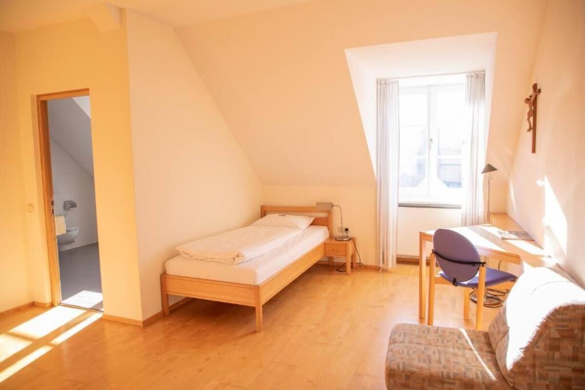 A bedroom with a bed, a desk, a chair, and a window.