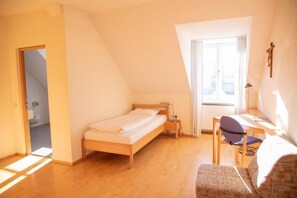 Un dormitorio con cama, escritorio, silla y ventana.