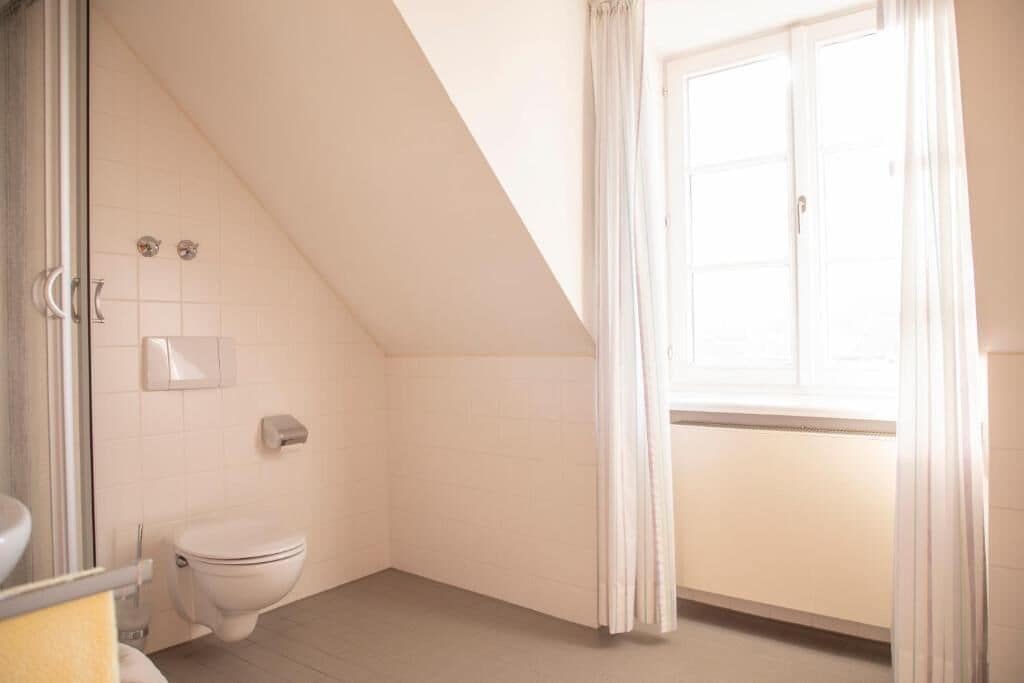 Ein Badezimmer mit Toilette, einem Handtrockner und einem fenster mit Vorhängen.