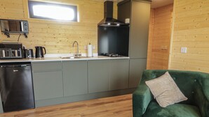 Cocina compacta con microondas, tostadora, cafetera y lavaplatos. Un sofá verde con un cojín se encuentra en la sala, y una revista está sobre la mesa de centro.