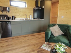 A compact kitchen with a microwave, toaster, coffee maker, and sink. A green sofa with a pillow is in the living area, and a magazine is on the coffee table. - Alken The Stag (Bushmills)