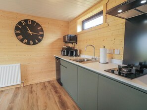 A modern kitchen with a wooden interior, a large wall clock, a built-in oven, and a window above the sink. - Alken The Stag (Bushmills)