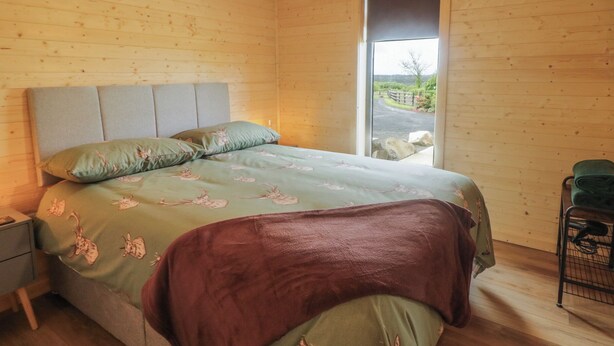 Un dormitorio con cama, mesita de noche, una silla y ventana con vistas al exterior.