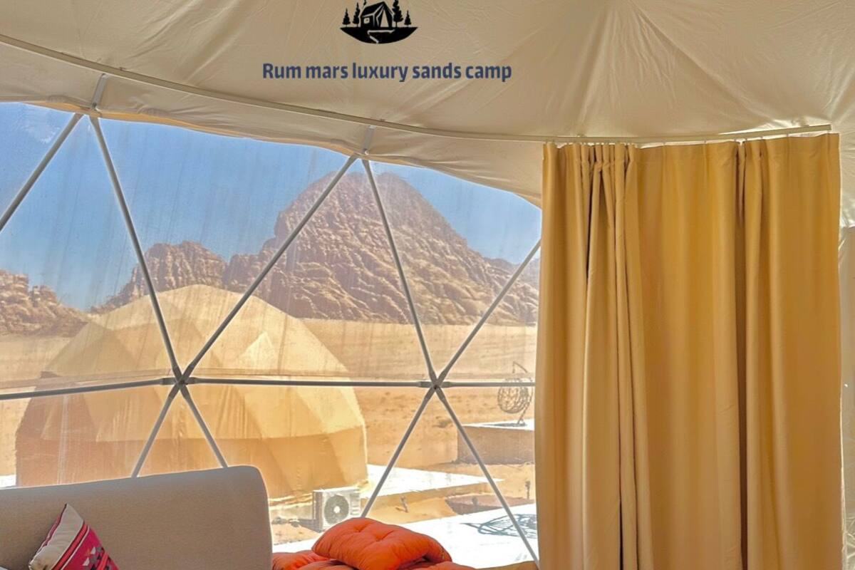 A luxury tent with a bed, sofa, and a view of mountains.