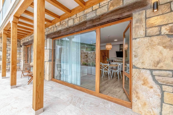 A covered outdoor area with stone walls, wooden beams, and a glass door leading to an interior dining space.