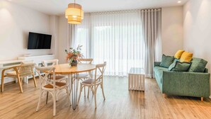 Een moderne woonkamer met een eethoek, een groene bank en een televisie aan de muur.