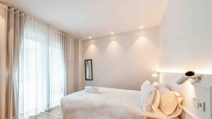 Een hotelkamer met een bed, gordijnen, een nachtkastje en een wandlamp.